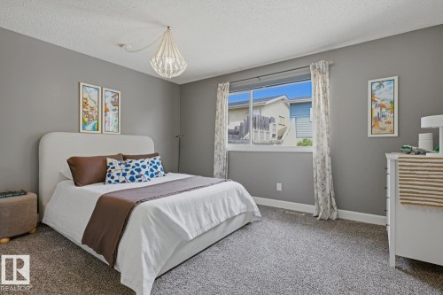 Inviting bedroom featuring gray wall paint, textured carpet flooring, and a large window with white trim - 3504 102 Avenue, Edmonton, AB 