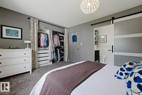 Carpeted bedroom with a sliding barn door entry to a bathroom, featuring built-in closet organization systems, a decorative ceiling light fixture, and a white dresser - 3504 102 Avenue, Edmonton, AB 