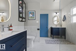Dual vanity bathroom featuring an enclosed shower, white marble-look wall and floor tiling, and dark blue cabinetry - 
