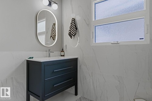 Vanity area featuring a dark-toned cabinet with a rectangular undermount sink, a chrome faucet, and a backlit oval mirror - 3504 102 Avenue, Edmonton, AB 