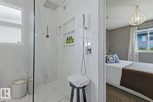 Walk-in shower with full-height marble-look tile surround, integrated shower niche, rainfall shower head, and an additional handheld shower fixture - 3504 102 Avenue, Edmonton, AB 