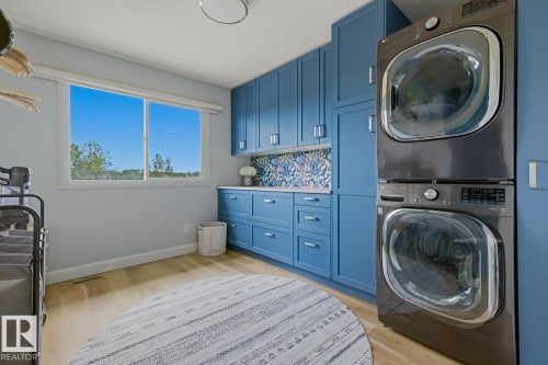Laundry room featuring extensive blue cabinetry, white countertops, stacked laundry appliances, and wood-finish flooring - 3504 102 Avenue, Edmonton, AB 