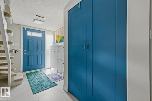Entryway featuring a paneled door with transom windows, light-toned floor tiling, and a carpeted staircase - 3504 102 Avenue, Edmonton, AB 