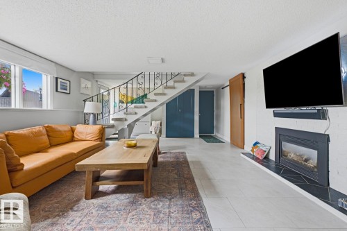 Living area featuring a white brick fireplace with a dark tile hearth, a wall-mounted TV, and light tile flooring - 3504 102 Avenue, Edmonton, AB 