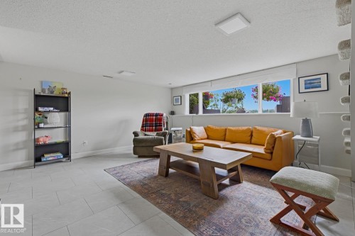 Spacious living area featuring light gray tile flooring and a bright window with exterior landscaping - 3504 102 Avenue, Edmonton, AB 