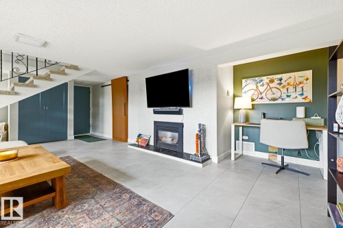 Living area featuring light-toned tile flooring, a built-in fireplace with a dark-toned hearth, under-stair storage cabinetry, a wood-finish barn door, and a dedicated desk alcove with an accent wall - 3504 102 Avenue, Edmonton, AB 