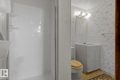 Bathroom featuring a white shower enclosure with built-in shelving, a vanity with a white cabinet, and a wall-mounted mirror with overhead lighting - 3504 102 Avenue, Edmonton, AB 