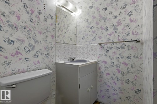 Compact bathroom featuring a white toilet, single vanity with a gray cabinet, and a wall-mounted mirror - 3504 102 Avenue, Edmonton, AB 