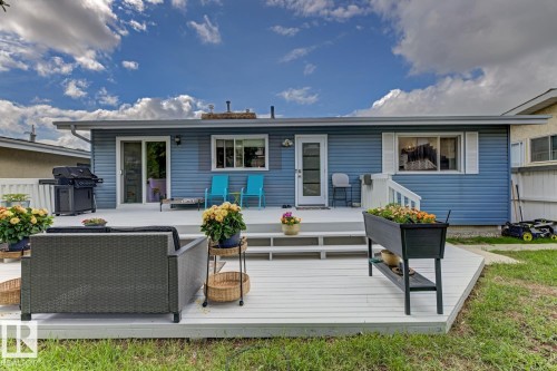 Expansive outdoor deck with white railing, blue siding exterior, sliding glass door, and a white entry door - 3504 102 Avenue, Edmonton, AB 