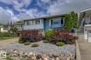 Exterior featuring light blue siding, a prominent bay window, white window shutters, and a rock garden with mature shrubs and trees - 3504 102 Avenue, Edmonton, AB 