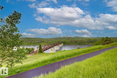 Paved pathway featuring natural land contours, expansive green space, a tranquil river, distant wooded areas, and a visible bridge structure - 3504 102 Avenue, Edmonton, AB 