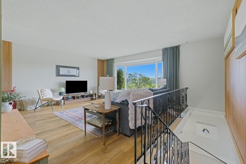 Living area featuring wood-finish flooring, a bay window, light-colored walls, and decorative vertical wall paneling - 3504 102 Avenue, Edmonton, AB 