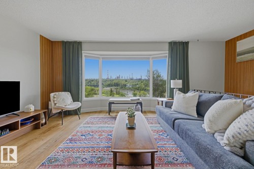 Living room with a prominent bay window, wood-finish flooring, and vertical wood paneling accents - 3504 102 Avenue, Edmonton, AB 