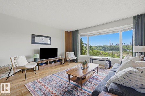 Bright living area featuring a large bay window with a scenic backdrop of trees and distant structures - 3504 102 Avenue, Edmonton, AB 