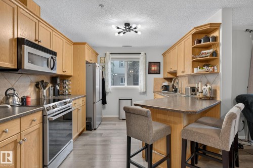 Kitchen featuring light wood cabinetry, stainless steel appliances, a breakfast bar, gray countertops, and wood-finish flooring - 122 279 Suder Greens Drive, Edmonton, AB 