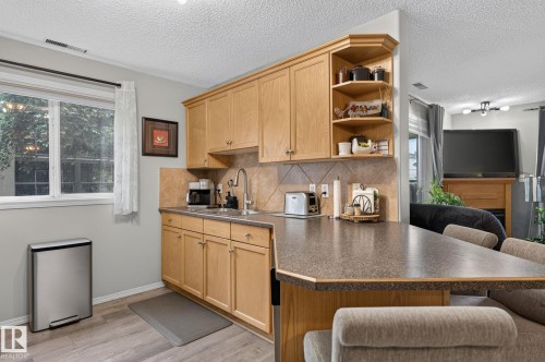 Kitchen featuring light wood cabinetry, a tiled backsplash, a double basin sink with a gooseneck faucet, a peninsula countertop, and wood-finish flooring - 122 279 Suder Greens Drive, Edmonton, AB 