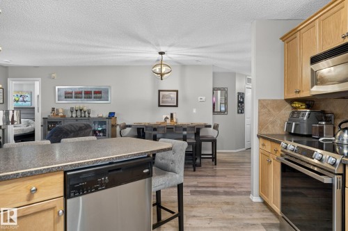 Kitchen featuring light wood cabinetry, stainless steel dishwasher, and a stone-finish countertop - 122 279 Suder Greens Drive, Edmonton, AB 