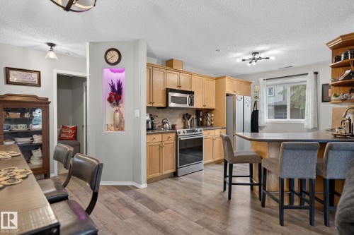 Kitchen featuring wood-finish flooring, light-toned cabinetry, stainless steel appliances, and a breakfast bar with seating - 122 279 Suder Greens Drive, Edmonton, AB 