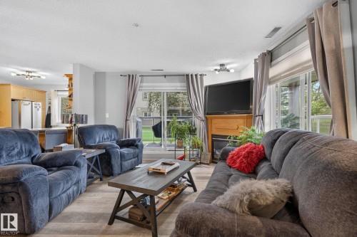 Living area featuring wood-finish flooring, a wood-surround fireplace, and a glass-paneled patio door - 122 279 Suder Greens Drive, Edmonton, AB 