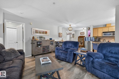 Open-concept living area featuring wood-finish flooring, light grey wall paint, and a textured ceiling - 122 279 Suder Greens Drive, Edmonton, AB 
