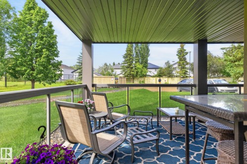 Covered outdoor patio featuring a slatted ceiling, sturdy pillars, and a glass-paneled railing - 122 279 Suder Greens Drive, Edmonton, AB 