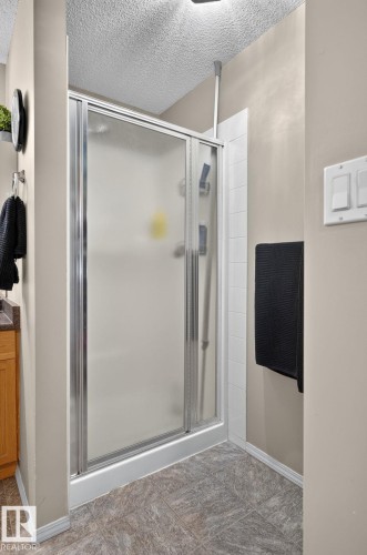 Enclosed shower with frosted glass and chrome framing, white tile surround, and textured ceiling - 122 279 Suder Greens Drive, Edmonton, AB 