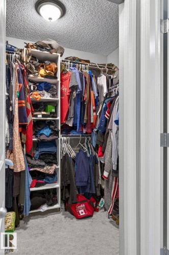 Walk-in closet featuring built-in shelving, hanging rods, and light gray carpeting - 122 279 Suder Greens Drive, Edmonton, AB 