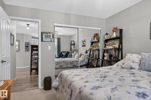 Bedroom featuring mirrored closet doors, neutral wall paint, and a textured ceiling - 122 279 Suder Greens Drive, Edmonton, AB 