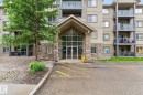 Multi-story building facade featuring a stone-clad entrance with a covered portico, large glass entry doors, and multiple private balconies with glass railings - 122 279 Suder Greens Drive, Edmonton, AB 