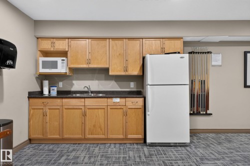 Kitchenette featuring light wood cabinetry, dark speckled countertops, and a stainless steel sink - 122 279 Suder Greens Drive, Edmonton, AB 