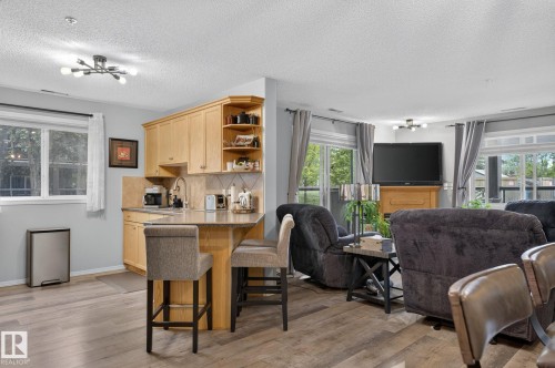 Open-concept living space featuring wood-finish flooring, a kitchen island with seating, natural wood cabinetry, a tiled backsplash, and recessed lighting - 122 279 Suder Greens Drive, Edmonton, AB 