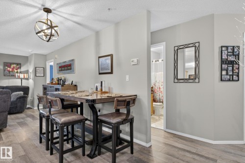 Dining area featuring wood-finish flooring, a contemporary chandelier, and light gray walls - 122 279 Suder Greens Drive, Edmonton, AB 