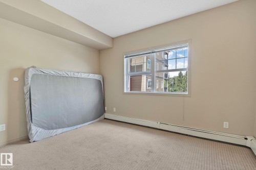 Carpeted room featuring a large window, neutral wall paint, white trim, and baseboard heating - 209 5280 Terwillegar Boulevard, Edmonton, AB - Indoor Photo Showing Other Room
