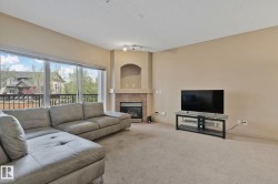 Living area with corner gas fireplace featuring a stone surround and mantel, sliding glass doors opening to a balcony, and neutral carpeting - 