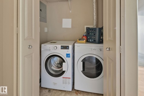 Dedicated laundry closet featuring a white front-load washer and dryer, wood-finish flooring, and a gray electrical panel - 209 5280 Terwillegar Boulevard, Edmonton, AB - Indoor Photo Showing Laundry Room