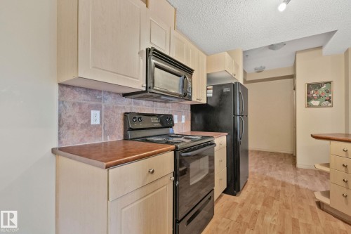 Kitchen featuring light wood-finish cabinetry, black appliances including a built-in microwave and range, and warm-toned countertops - 209 5280 Terwillegar Boulevard, Edmonton, AB - Indoor Photo Showing Kitchen