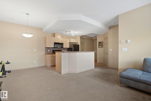 Open-concept living space featuring a kitchen with light wood-finish cabinetry, black appliances, and a breakfast bar - 209 5280 Terwillegar Boulevard, Edmonton, AB - Indoor Photo Showing Kitchen