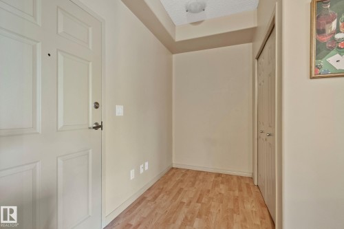 Entryway featuring wood-finish flooring, a paneled door with brushed nickel hardware, and a built-in closet with bifold doors - 209 5280 Terwillegar Boulevard, Edmonton, AB - Indoor Photo Showing Other Room