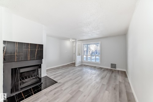 Spacious interior featuring a modern fireplace with a black and gold veined surround, light wood-finish flooring, a large window, and light-toned walls - 23 1503 Mill Woods Road E, Edmonton, AB 