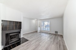 Spacious interior featuring a modern fireplace with a black and gold veined surround, light wood-finish flooring, a large window, and light-toned walls - 