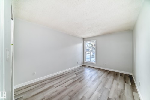 Spacious room featuring wood-finish flooring, light grey wall paint, white baseboards, and a window with white trim - 23 1503 Mill Woods Road E, Edmonton, AB 