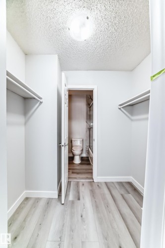 Walk-in closet featuring light wood-finish flooring, white walls, and built-in shelving - 23 1503 Mill Woods Road E, Edmonton, AB 