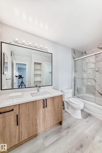 Bathroom featuring a wood-finish vanity with a white countertop, an undermount sink, and a large framed mirror - 23 1503 Mill Woods Road E, Edmonton, AB 