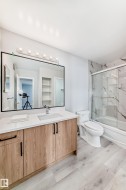 Bathroom featuring a wood-finish vanity with a white countertop, an undermount sink, and a large framed mirror - 