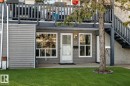 Exterior entry featuring grey horizontal siding, white trim windows, an illuminated outdoor sconce, a front door with a storm door, and a manicured lawn - 23 1503 Mill Woods Road E, Edmonton, AB 