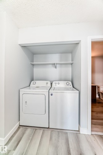 Dedicated laundry alcove featuring a white washer and dryer pair, an integrated storage shelf, and light wood-finish flooring - 23 1503 Mill Woods Road E, Edmonton, AB 