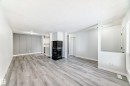 Spacious living area featuring wood-finish flooring, a black-tiled fireplace with hearth, and a decorative accent wall - 23 1503 Mill Woods Road E, Edmonton, AB 