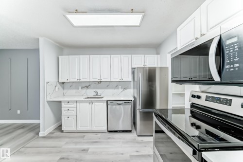 Kitchen featuring white cabinetry, stone-look countertops, stainless steel appliances, and wood-finish flooring - 23 1503 Mill Woods Road E, Edmonton, AB 