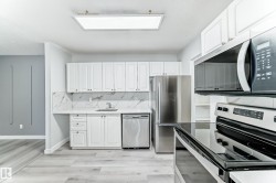 Kitchen featuring white cabinetry, stone-look countertops, stainless steel appliances, and wood-finish flooring - 