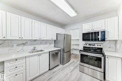 Kitchen featuring bright white cabinetry, stainless steel appliances, marble-patterned backsplash, light wood-finish flooring, and ample counter space - 